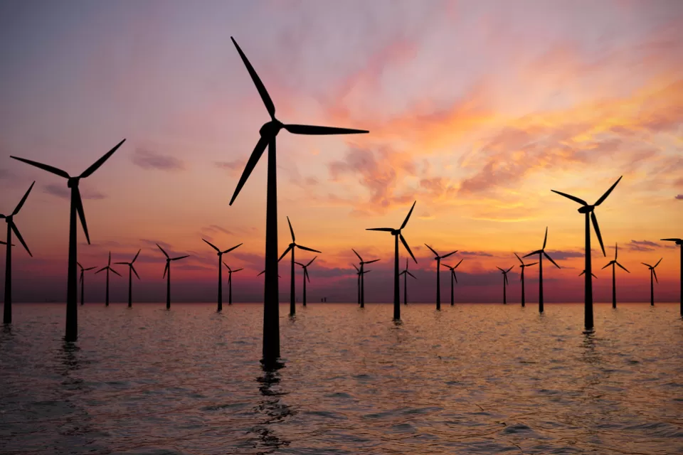 Offshore wind turbines in water against a sunset sky